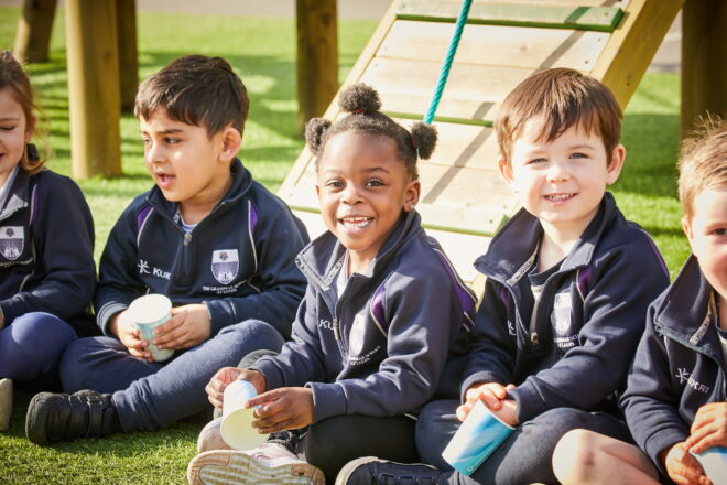 Nursery pupils are sitting outside in front of some play equipment